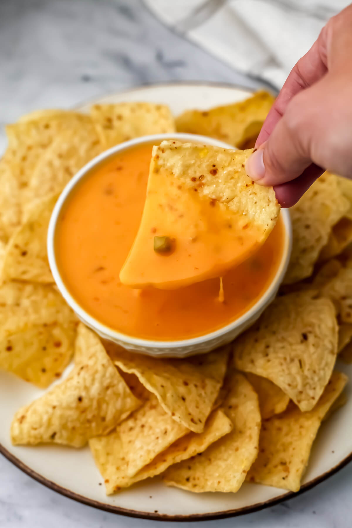 Easy vegan queso dip in a white bowl with a corn chip being dipped into it.