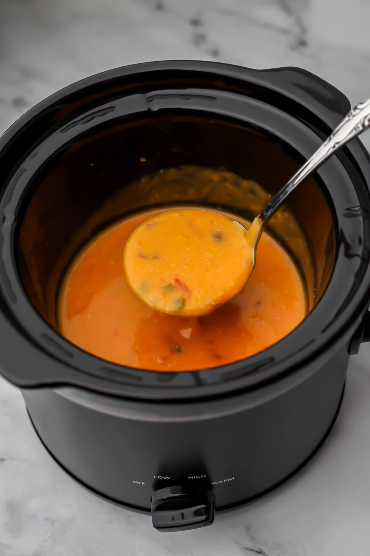 Easy vegan queso in a slow cooker being scooped up by a spoon.