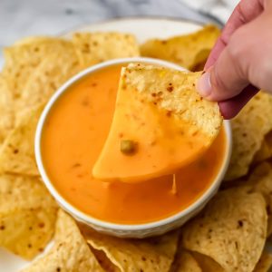 Easy vegan queso dip in a white bowl with a chip being dipped into it.