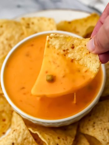 Easy vegan queso dip in a white bowl with a chip being dipped into it.