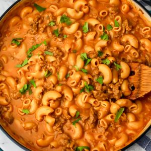 Vegan hamburger helper in a blue skillet being stirred with a wooden spoon.
