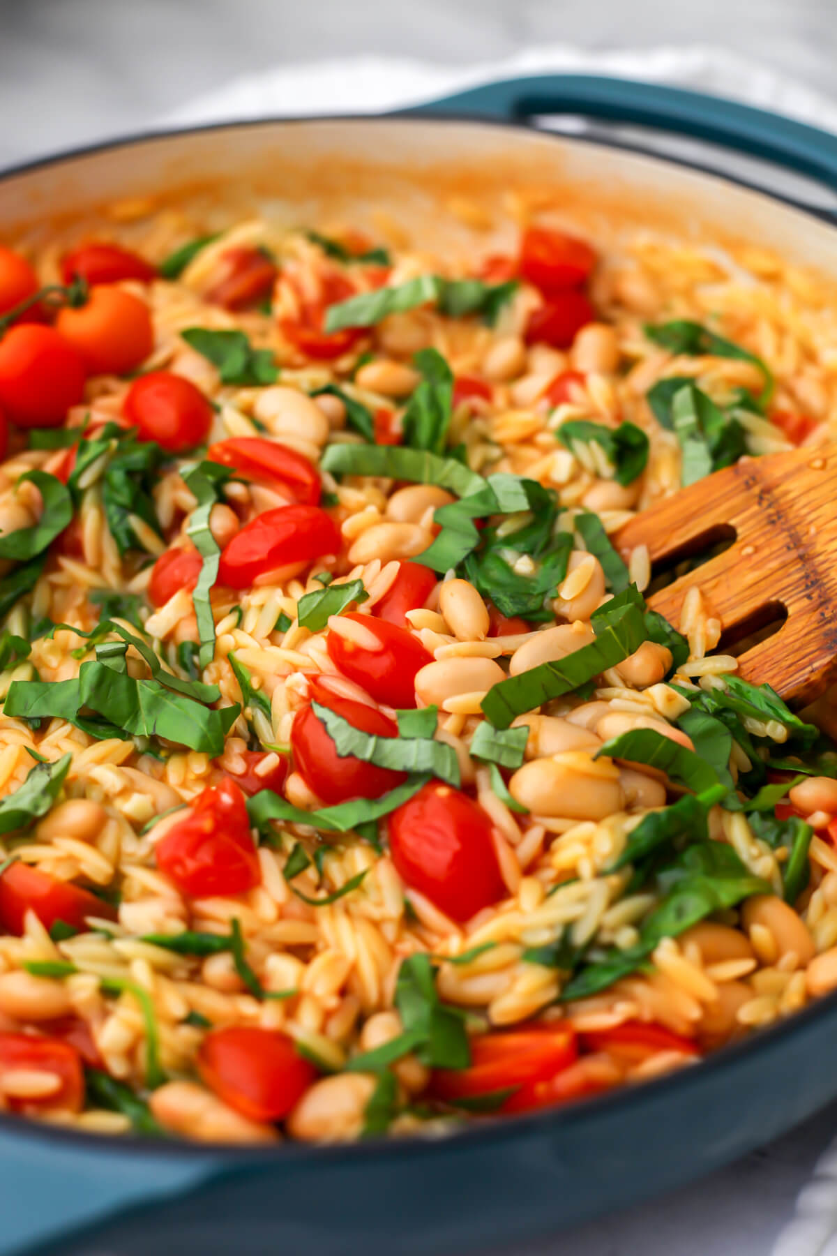 Vegan cherry tomato orzo with white beans in a blue iron skillet.