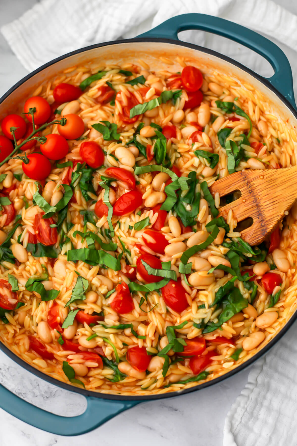 A top view of a skillet full of cherry tomato orzo with white beans.