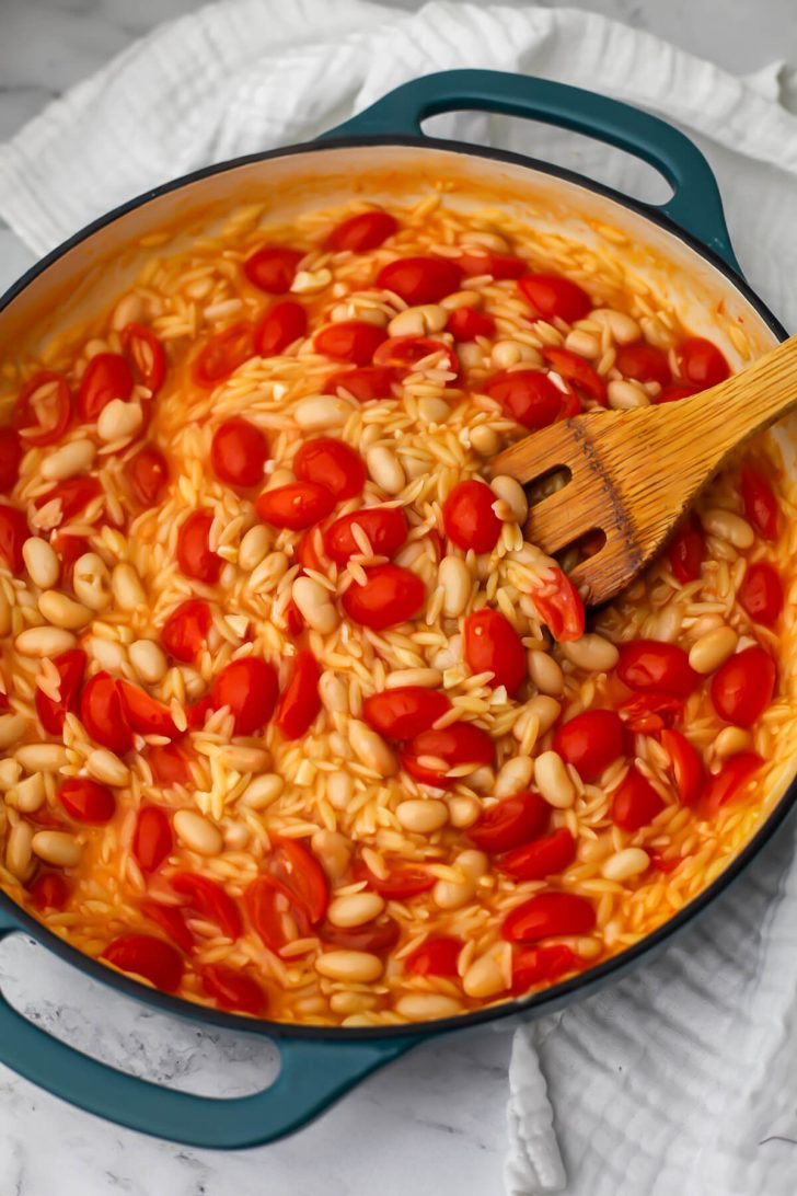 Cherry tomato orzo with white beans cooking in a blue skillet.