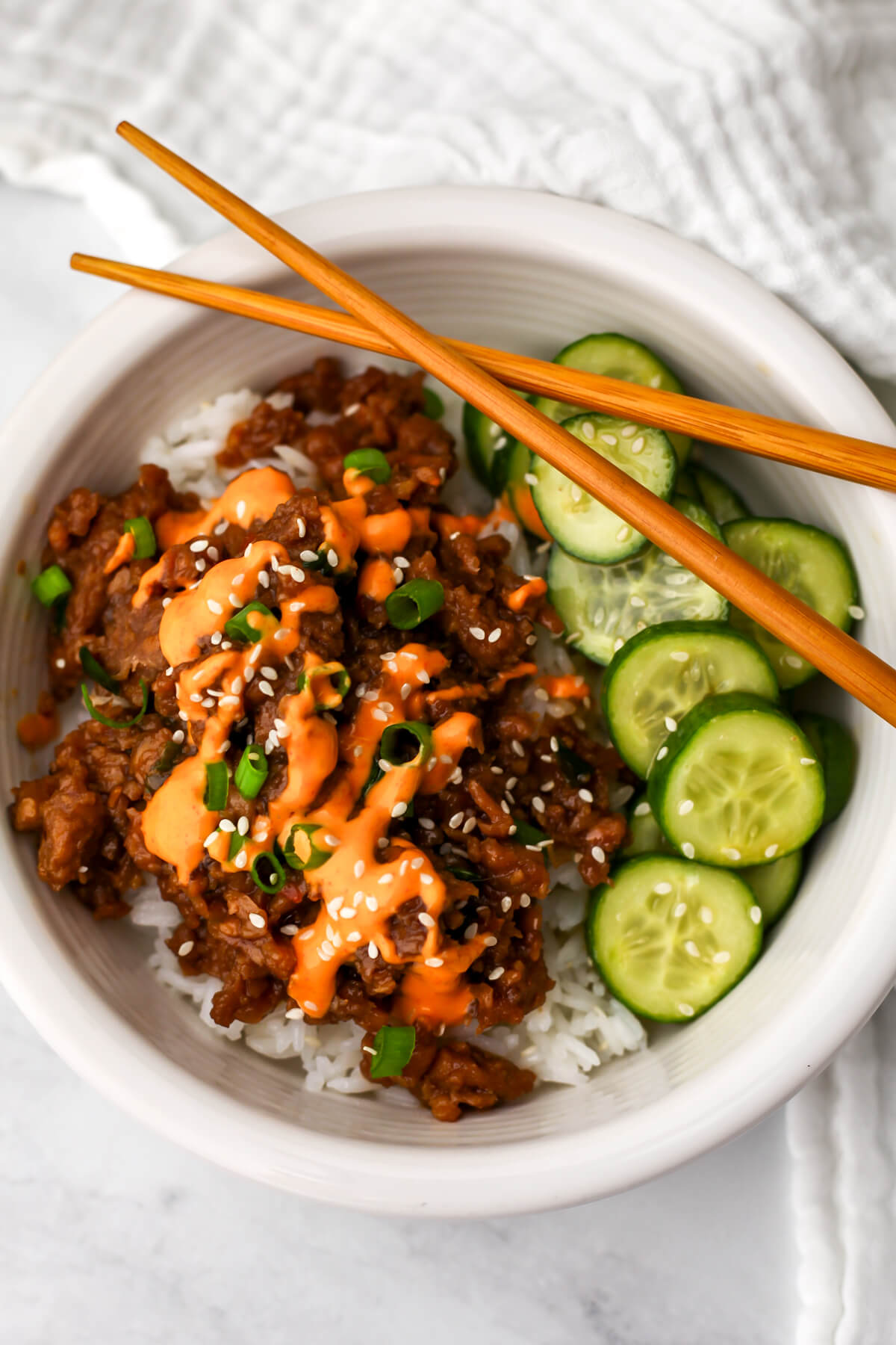 A top view of a vegan Korean beef bowl served over rice and drizzled with vegan yum yum sauce with cucumbers on the side.