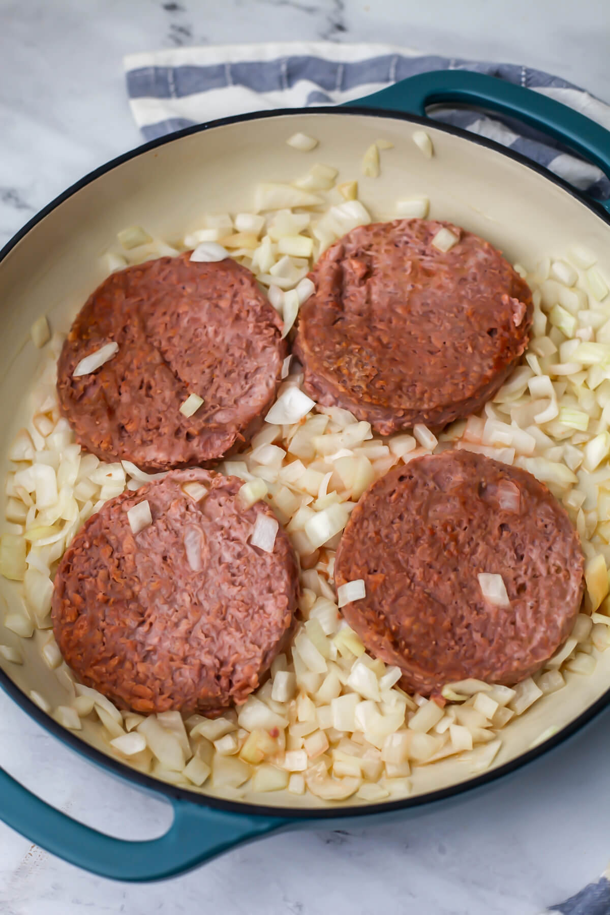 Onions sauteing in a frying pan with 4 vegan burger patties added to it.