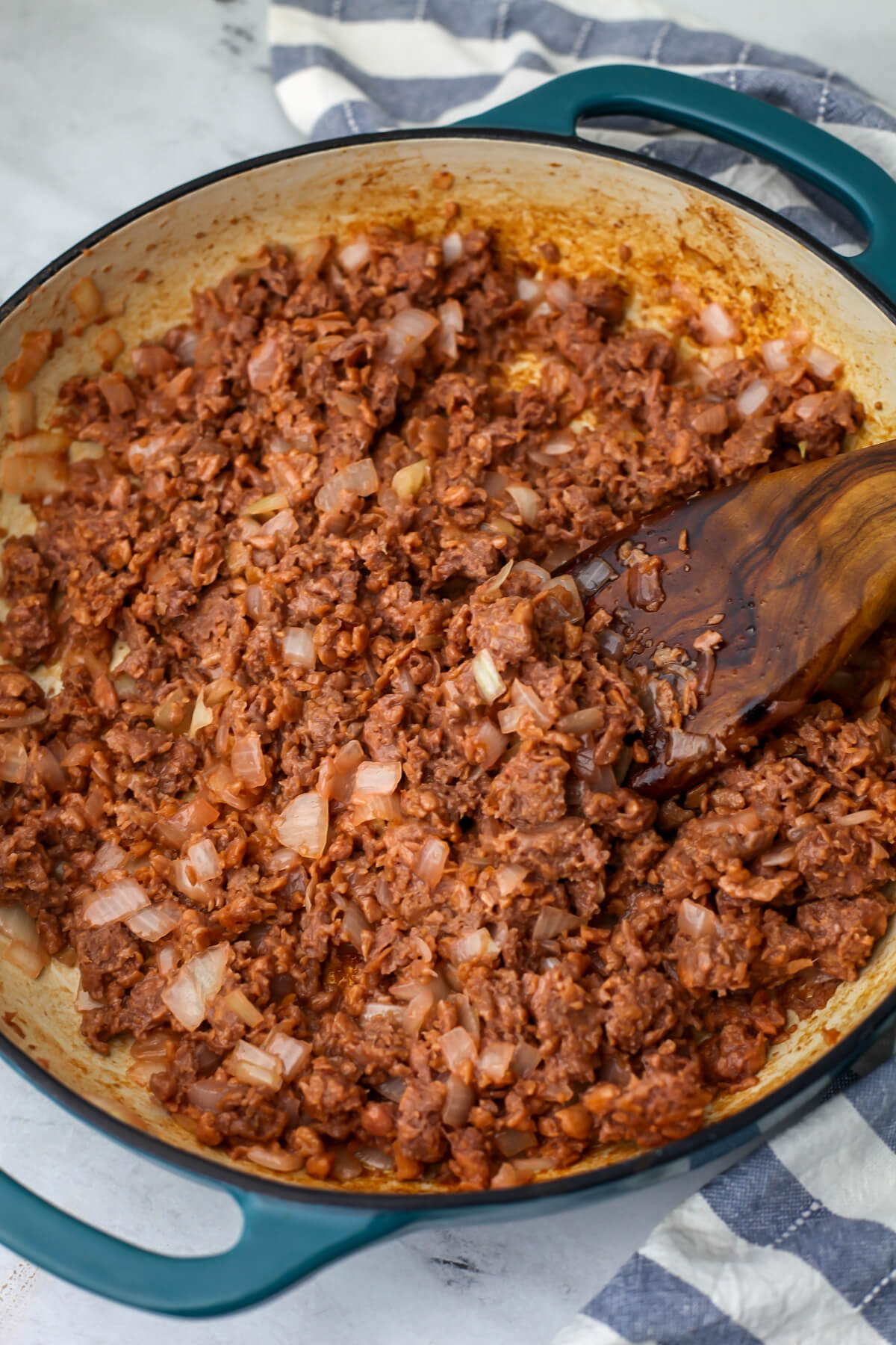 Vegan burgers cooked with onions in a large skillet.