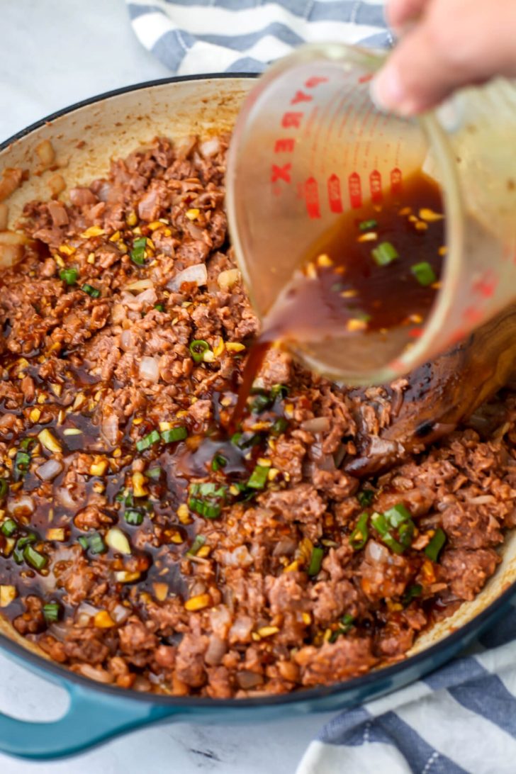Pouring the marinade over the cooked vegan beef and onions.