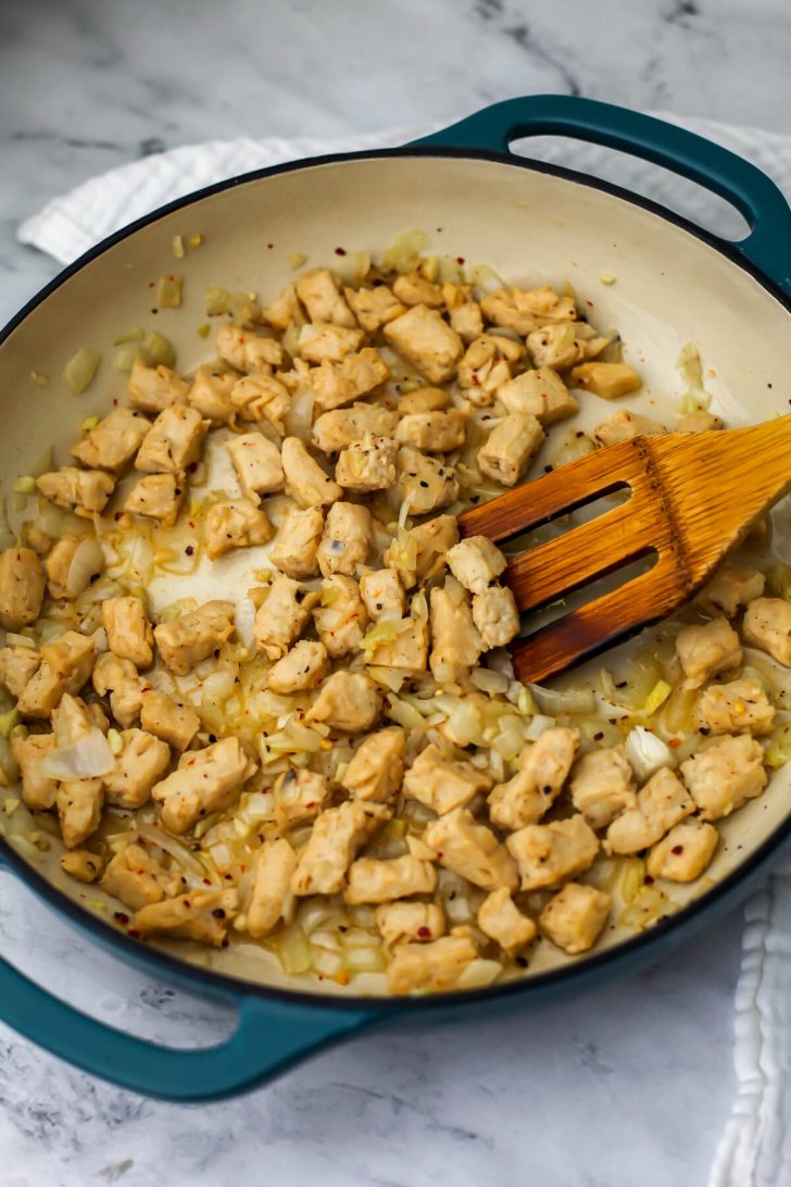 Onions, garlic, and vegan chicken sautéing in a skillet.
