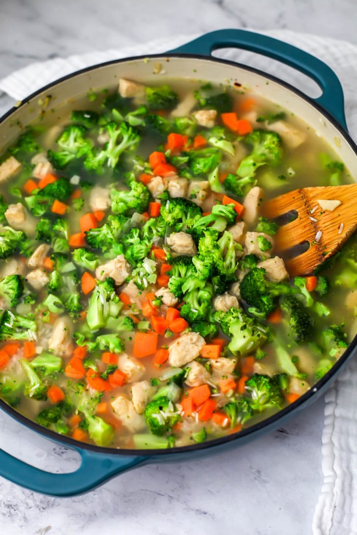 Rice, broth, vegan chicken, broccoli, and carrots cooking in a skillet.