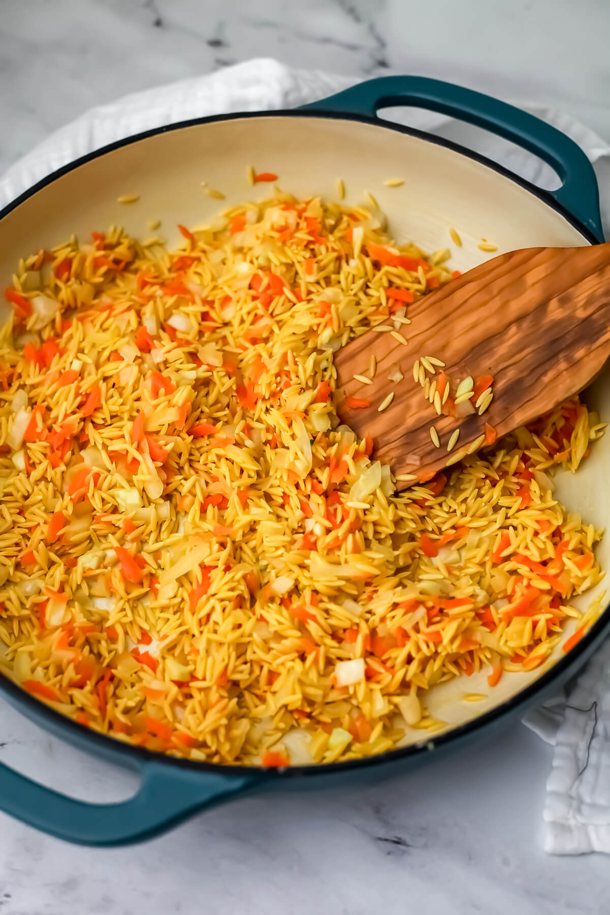 Orzo added to the onions and carrots in a skillet.