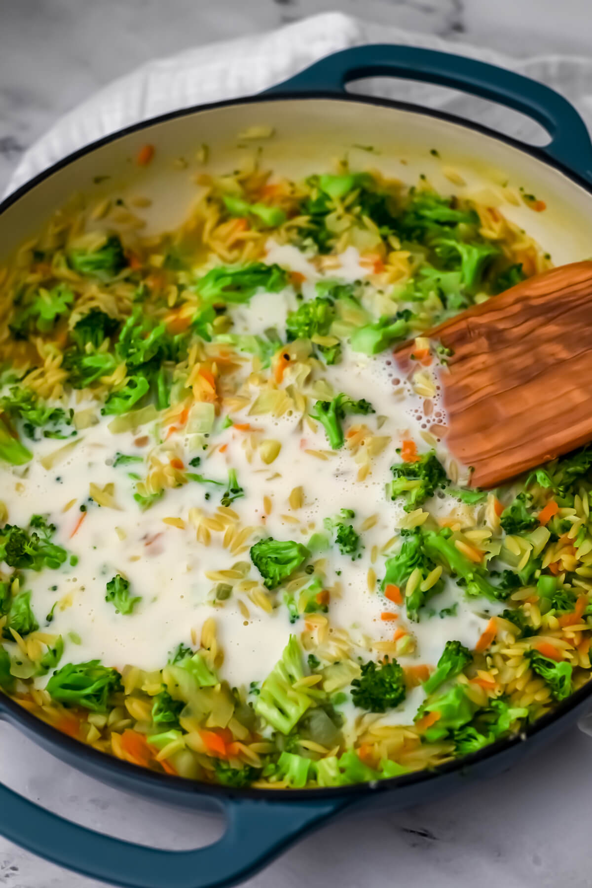 Plant-based milk added to the broccoli and orzo in a skillet.