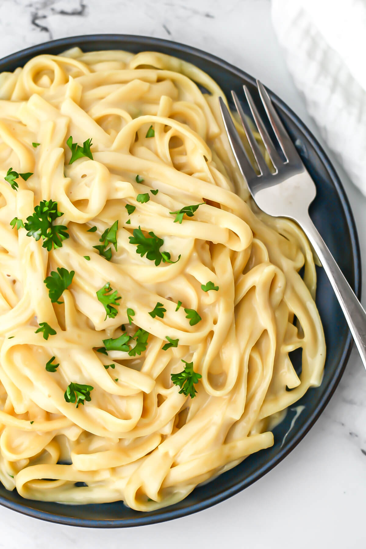 A blue plate filled with vegan oat milk alfredo sauce over fettuccini topped with parsley.