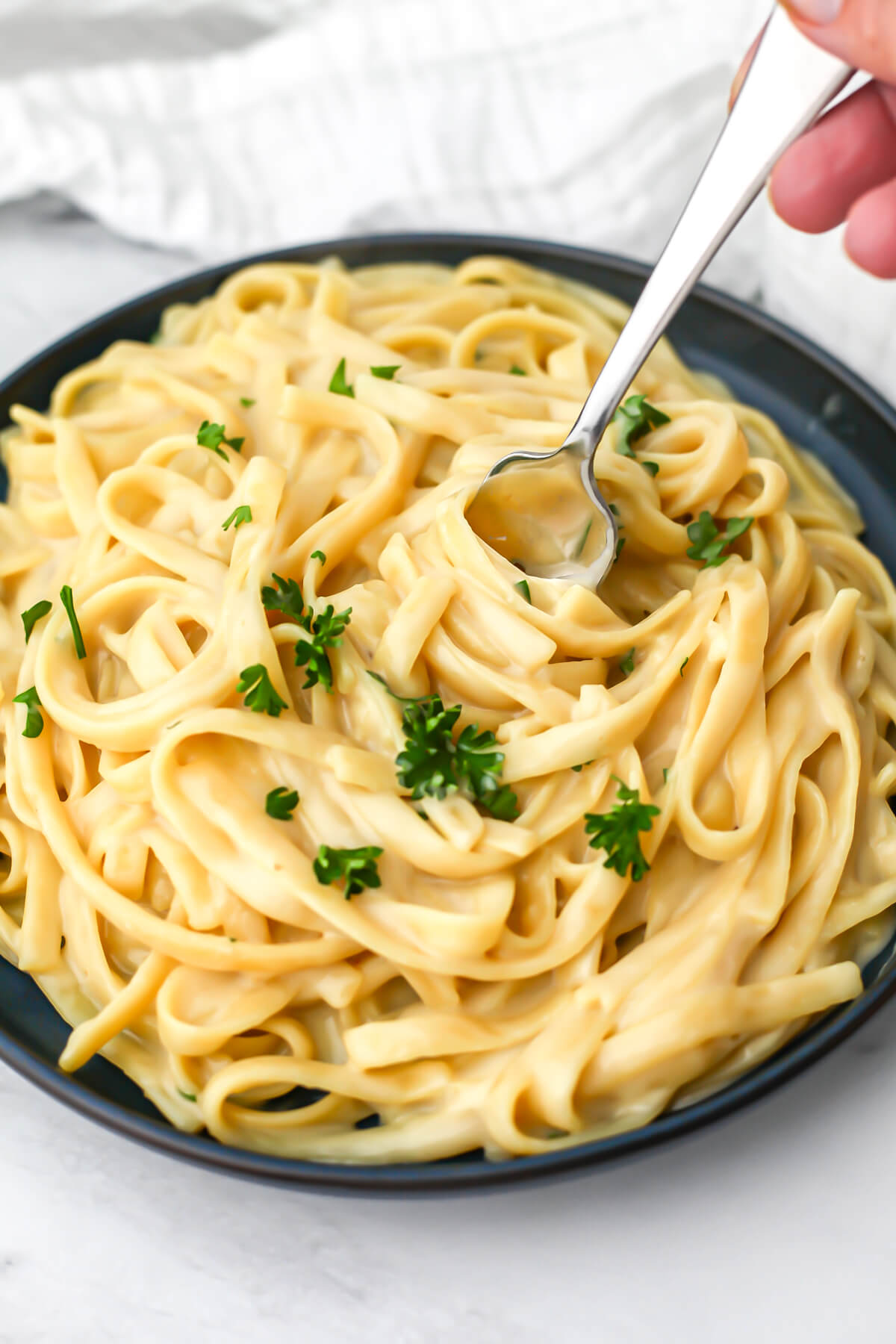 A plate of oat milk fettuccini Alfredo with a fork in it.