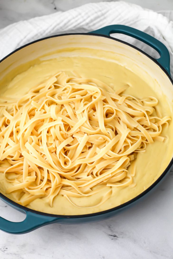 Cooked fettuccini noodles added to oat milk alfredo sauce.