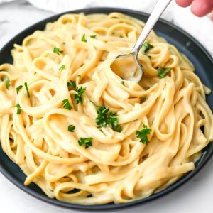 A plate of vegan oat milk alfredo sauce over noodles with a fork in it.