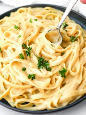 A plate of vegan oat milk alfredo sauce over noodles with a fork in it.