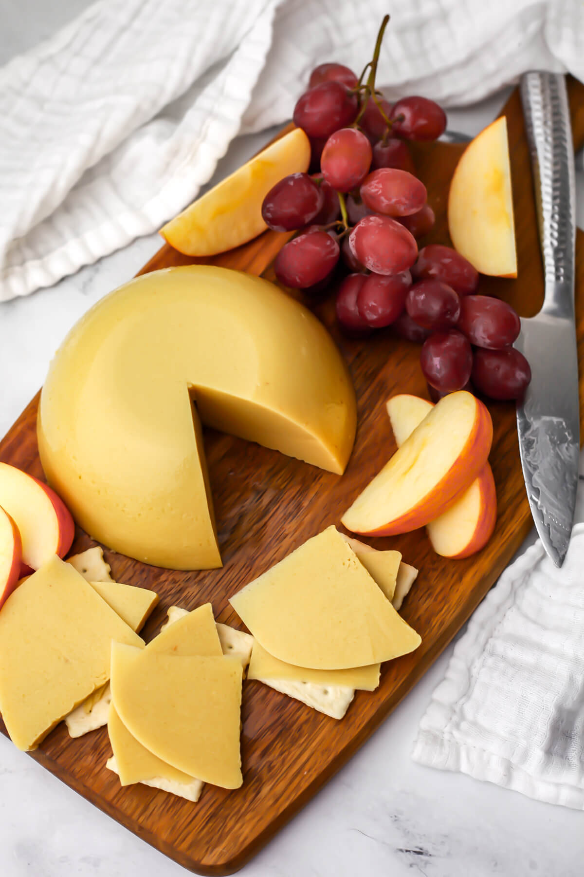 A top view of a cutting board filled with oat milk cheese, red grapes, and apple slices.